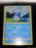 Close-up photo of single Marill Pokémon trading card showing detailed artwork of a blue knitted Marill with mountain background. Card text and attributes visible.