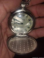 Front view of open pocket watch showing mother of pearl dial with black numerals and hands, branded 'Suisse' with quartz movement.