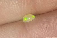 Close-up of an orange opal gemstone resting on a fingertip showing iridescent green flecks within the stone.