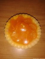 Top view of the wax candle showing the peach slice design inside a scalloped edged mold, sealed with clear wax or plastic dome.