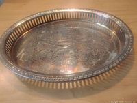 Photo of oval silver plated brass serving tray showing etched floral pattern and pierced edge detail, viewed at an angle.