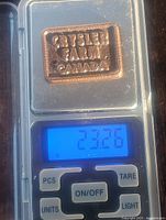 Solid bronze rectangular ingot bar on a digital scale showing weight of 23.26 grams.