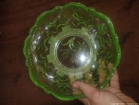 View of antique uranium glass bowl displaying bright green color with floral pressed pattern and scalloped edges, held in hand for scale.
