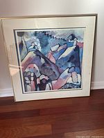 Full view of framed abstract print showing the composition of colorful geometric and house forms in blues and purples.