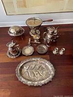 Wide view of the assorted antique silver tableware items arranged on wooden floor for identification and condition assessment.