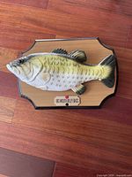 Full view of Big Mouth Billy Bass mounted on wooden plaque on wood floor.