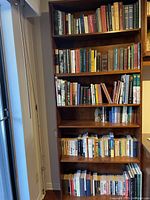 Full view of tall wooden bookshelf filled with used books across six shelves.
