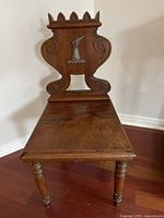 Front angle view of antique wooden chair showing carved backrest with hand and dagger motif and crown-like top detail.