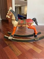 Side view of the traditional wooden rocking horse showing multicolor paint and horse details on hardwood floor.