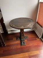 Side view of antique circular wooden table showing carvings and base