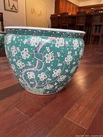 Side view showing turquoise and white ceramic flower pot with detailed cherry blossom branch design around the exterior.