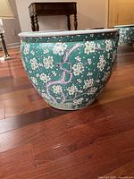 Side view of the ceramic flower pot showing green background with white cherry blossom pattern and some tarnishing.