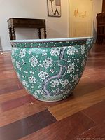 Side view of the ceramic flower pot showing green exterior with white blossoms and tree branch motif.