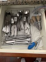 Overhead view of open drawer containing metal cutlery and kitchen utensils in a metal organizer tray.