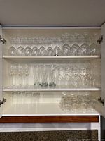 Full closet shelf showing 44 clear glasses including multiple types arranged on three shelves.