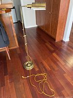Full view of the brass floor lamp showing adjustable pole, round base and yellow electrical cord coiled on the floor.