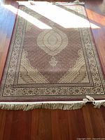 Full view of rectangular oriental area rug laid on wooden floor, showing fringe and intricate border design.
