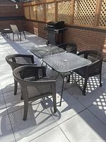 View of outdoor patio set showing two glass-top tables and four black wicker-style chairs in sunlight