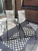 Two lounge chairs with beige mesh and black metal frames on patio, shadow pattern from lattice above.