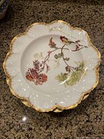 Top view of a single porcelain plate showing floral design and scalloped gold rim