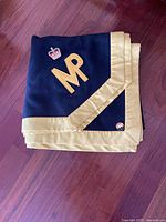 Folded navy blue and gold saddle blanket showing embroidered crown and MP initials