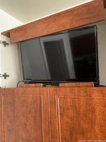 Small black Insignia TV placed on wooden cabinet, showing front view with screen off and cables visible.