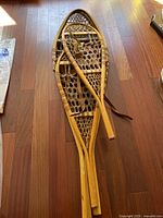 Pair of antique wooden snowshoes laid on wooden floor showing full length and leather straps