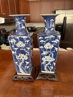 Front view of two blue and white square vases on carved wooden stands