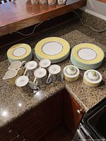 Photo of entire dinnerware set including stacked plates, mugs, sugar bowl, and creamer on countertop.