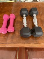 Photo of two pairs of dumbbells on a wooden surface, pink neoprene pair and black hex pair.
