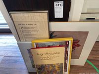 Framed and unframed wall art pieces leaning against a window sill including a poem print titled 'Deed Mate in the Pear Tree' and floral garden prints.