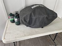 Weber barbecue with propane canisters and protective cover on resin folding table