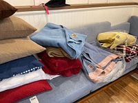 Photo of several stacked cushions along with multiple folded blankets including wool and plush types on a blue couch.