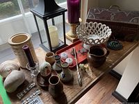 Wide view of the full lot showing antique chest, ceramic bowl, lantern, various candle holders, and other decorative items on a wooden table.