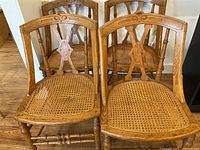 Four wooden spindle leg chairs with cane woven seats and carved wooden backrests. Damage and scratches visible on the cane seats and wooden frames.