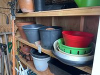 Shelves with terra-cotta and resin planter pots in various sizes and colors with some pot bases and saucers.