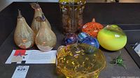 Wide view of the entire lot showing three large amber glass pears, a textured amber glass vase, orange pumpkin-shaped glass piece, yellow-green rounded glass piece, and four assorted glass spheres