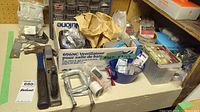 Photo of various hardware items including hammers, C-clamps, metal file, rasp, and sorting box with plastic drawers containing screws and nails.