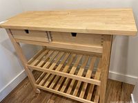 Front view of kitchen island showing butcher block top, two drawers, and two slatted shelves.