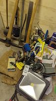 View of tools including pickaxe, crowbar, axe, paint brushes and gloves alongside Husky work light and other painting supplies.
