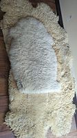 Large rectangular off-white sheepskin rug with thick curly wool, placed on wooden floor, partially covered by smaller rug