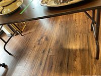 Photo showing the table top surface with some silver trays placed on it to illustrate condition of table top including edge damage and scratches.