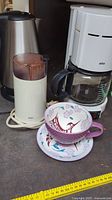 Photo showing Braun coffee maker, Braun coffee grinder, stainless steel kettle, and decorative cup and saucer