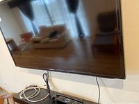 Samsung 40 inch TV mounted on wall with power cable and remote placed below on shelf.