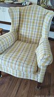Overview of wing back chair angled front view showing plaid upholstery and armrests.
