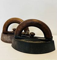 Front angle showing two antique sad irons with wooden handles and cast iron bases.