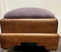 Side view of antique wooden footstool showing dark brown wood, purple velvet cushion, and glass foot supports.