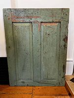 Front view of the antique wooden door section showing two recessed panels with green paint and areas of exposed wood and old paint underneath.