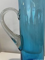 Close-up of clear handle attached to blue glass pitcher body.