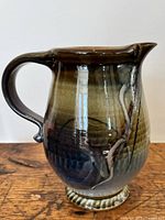 Front side view showing round body, spout, handle, and layered dark earth tone glazes